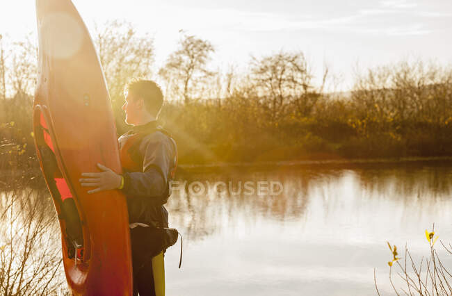 Jovem homem segurando caiaque pelo lago — Fotografia de Stock