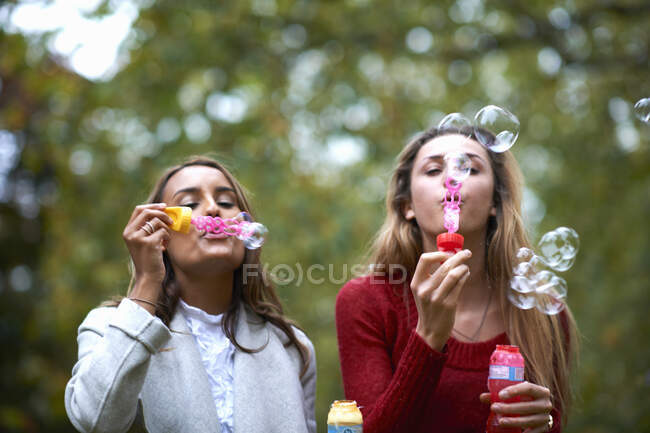 Dos amigas jóvenes soplando burbujas en el parque - foto de stock