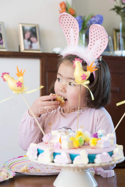 Menina jovem vestindo orelhas de coelho, comer bolo — Fotografia de Stock