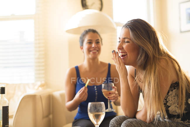 Deux jeunes femmes ayant des filles nuit dedans, boire et rire — Photo de stock