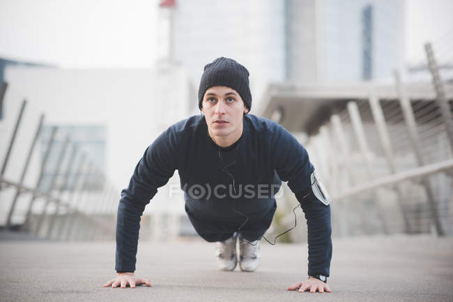 Young male runner doing press ups on city footbridge — Stock Photo