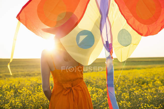 Vista trasera de mujer adulta media en brazo de campo de canola levantado sosteniendo cometa - foto de stock