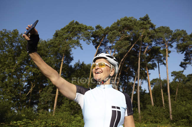 Ciclista maduro tomando selfie ao lado da floresta — Fotografia de Stock