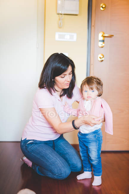 Mid adult woman putting on toddler daughters cardigan — Stock Photo