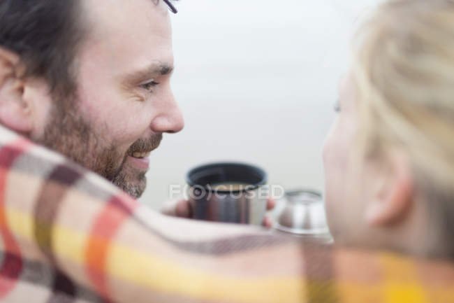 Couple on beach drinking hot drink from flask and smiling — Stock Photo