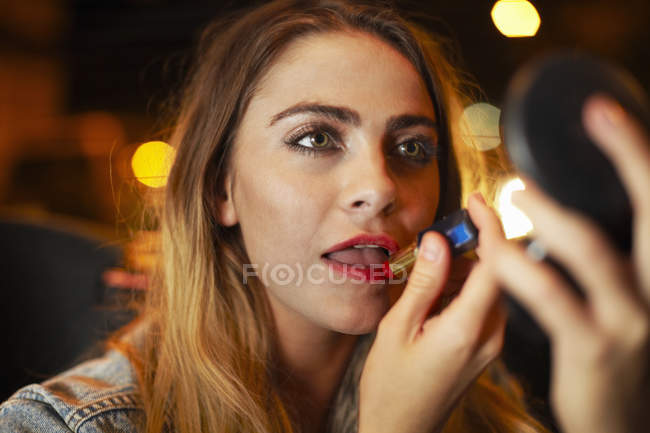 Beautiful young woman applying lipstick in city taxi at night — Stock Photo