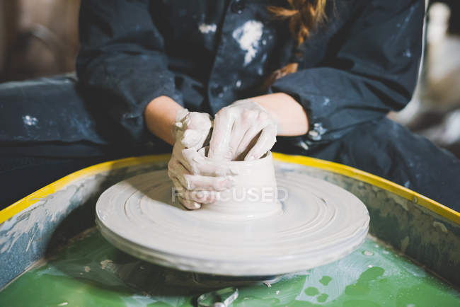 Обрезанный вид молодой женщины, сидящей за гончарным колесом и делающей глиняный горшок — стоковое фото
