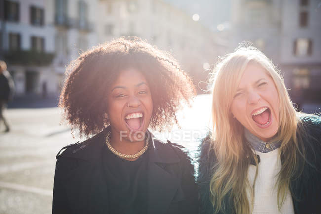 Retrato de dos amigas riendo en la plaza de la ciudad - foto de stock
