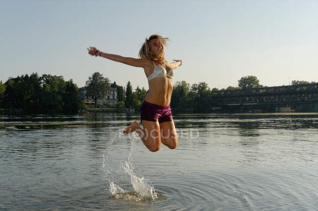 Partially dressed mid adult woman, jumping in lake — Stock Photo