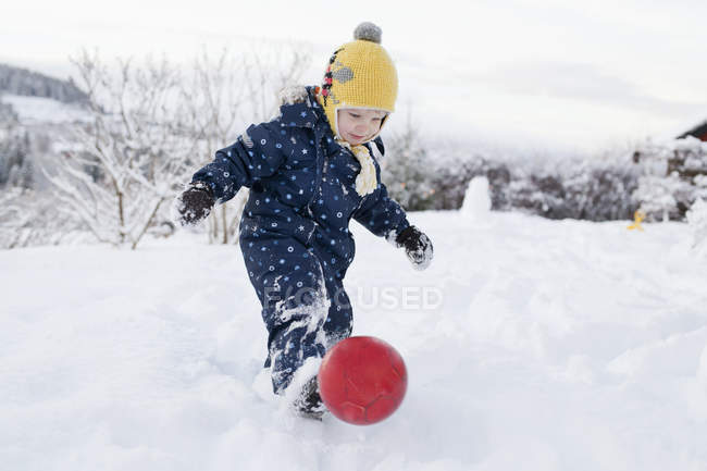 Маленький хлопчик штовхає м'яч у засніженій сільській місцевості — стокове фото