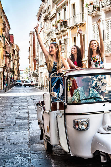 Three young women waving from open back seat of Italian taxi, Cagliari, Sardinia, Italy — Stock Photo