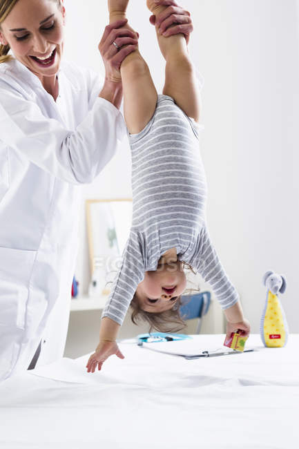 Pediatra tenendo bambino ragazzo a testa in giù — Foto stock