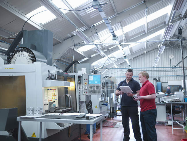 Engineers discussing work in front of CNC machines in engineering factory — Stock Photo