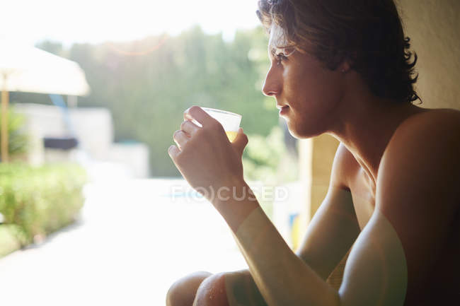 Jeune homme buvant une boisson gazeuse sur chaise patio — Photo de stock