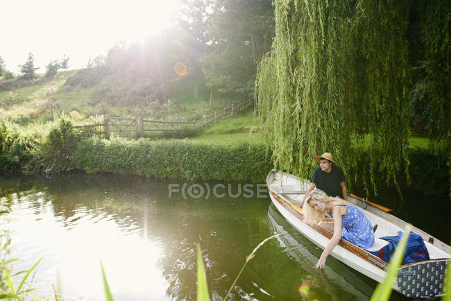 Jeune femme avec petit ami touchant l'eau de la rivière bateau à rames — Photo de stock