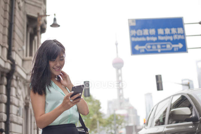 Joven empresaria, usando smartphone, al aire libre, Shanghai, China - foto de stock