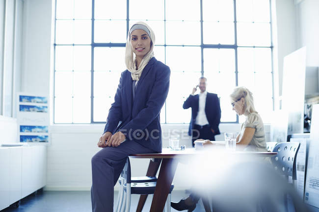 Portrait of young businesswoman sitting on office desk — Stock Photo