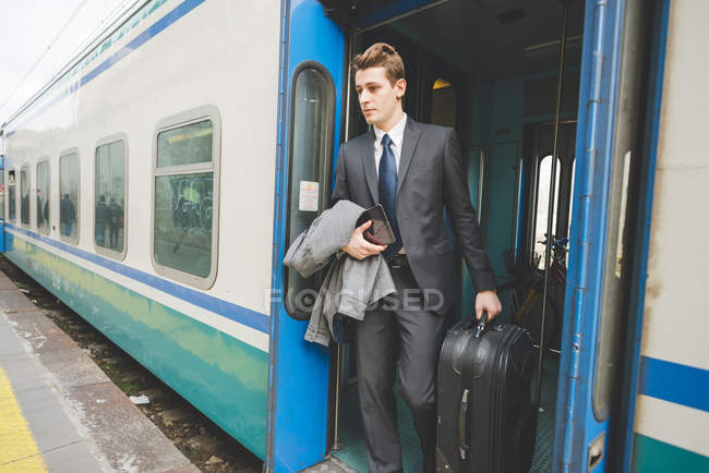 Junger Geschäftsmann steigt mit Koffer aus Zug aus. — Stockfoto