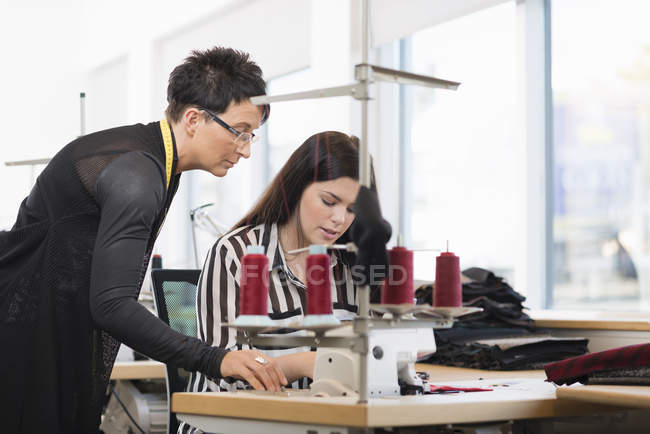 Дві швачки дивиться вниз на швейну машинку в майстерні — стокове фото