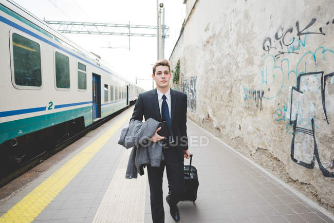 Young businessman commuter walking along railway platform with suitcase. — Stock Photo