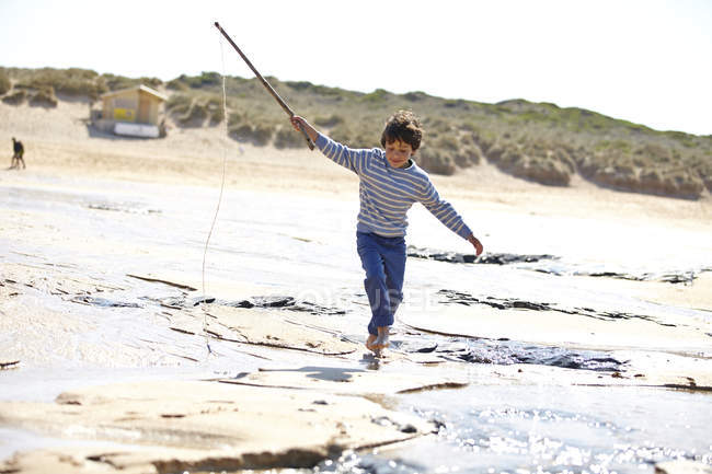 Junge läuft mit Stock am Sand entlang — Stockfoto