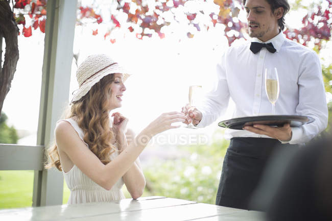 Serveur servant du champagne à une jeune femme dans un restaurant de jardin — Photo de stock