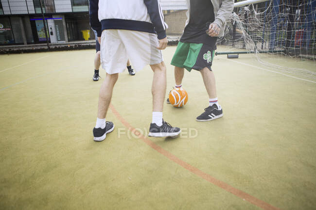 Group of adults playing football on urban football pitch, low section — Stock Photo