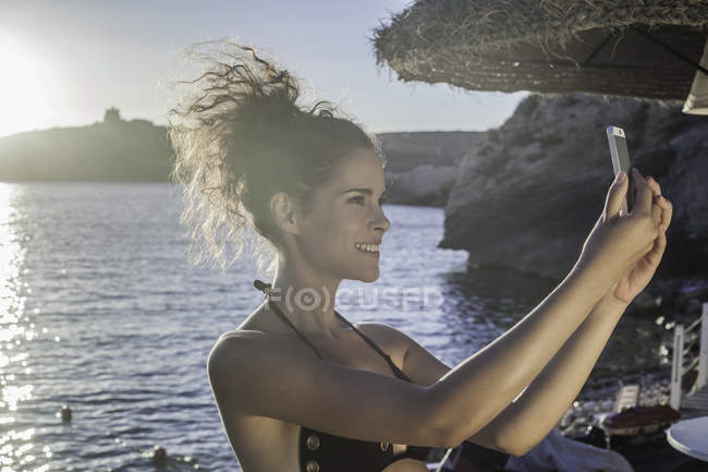 Вид сбоку молодой женщины, делающей селфи — стоковое фото