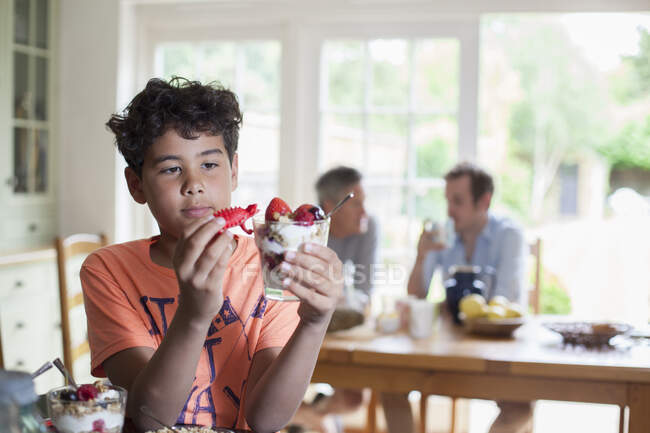 Grandson holding breakfast granola, father and grandfather sitting behind at kitchen table — Stock Photo