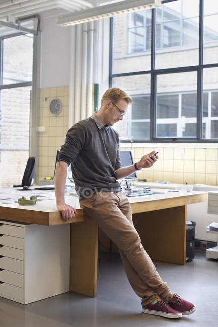 Мужчина дизайнер смотрит на смартфон в креативном офисе — стоковое фото