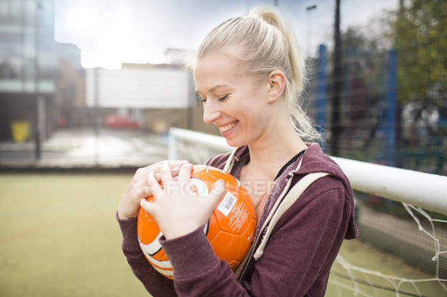 Молода жінка тримає футбол, посміхаючись — стокове фото