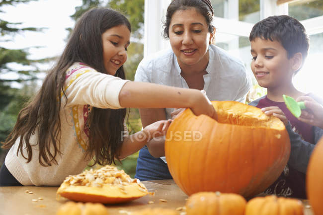 Madre e hijos ahuecando la calabaza en el comedor - foto de stock