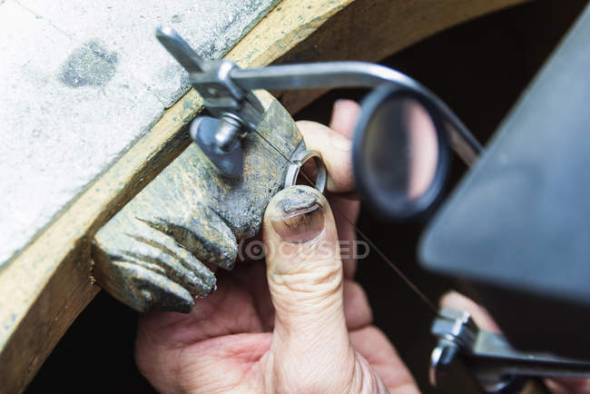 Close up of jewellery craftsmans hand sawing platinum ring — Stock Photo