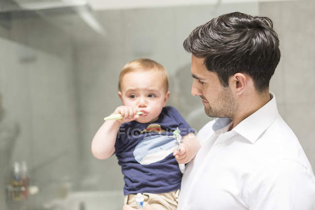Батько тримає молодого сина, коли син чистить зуби — стокове фото