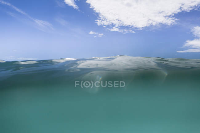 Величественный подводный вид на спокойную морскую воду и голубое небо с белыми облаками — стоковое фото