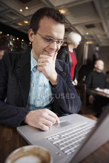 Бизнесмен использует ноутбук в интерьере кафе с людьми в фоновом режиме — стоковое фото