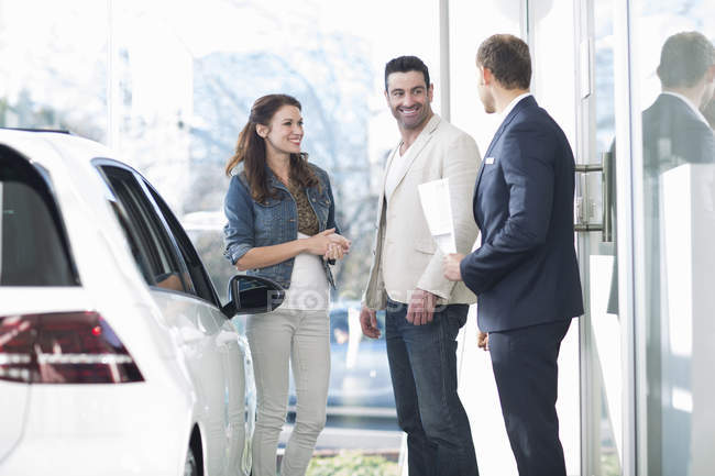 Salesman and mid adult couple chatting in car dealership — Stock Photo