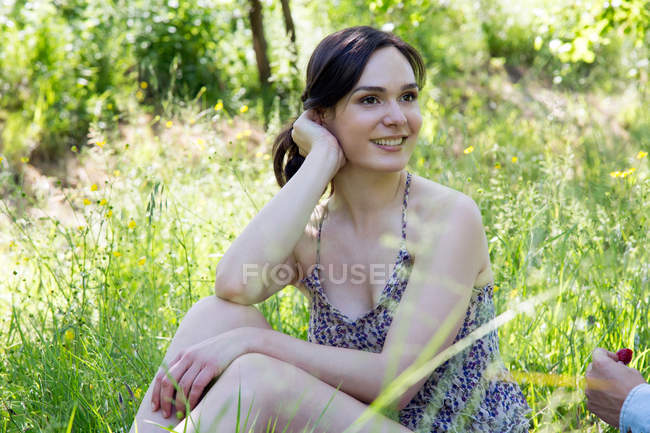 Mujer joven sentada en la hierba mirando hacia otro lado sonriendo - foto de stock