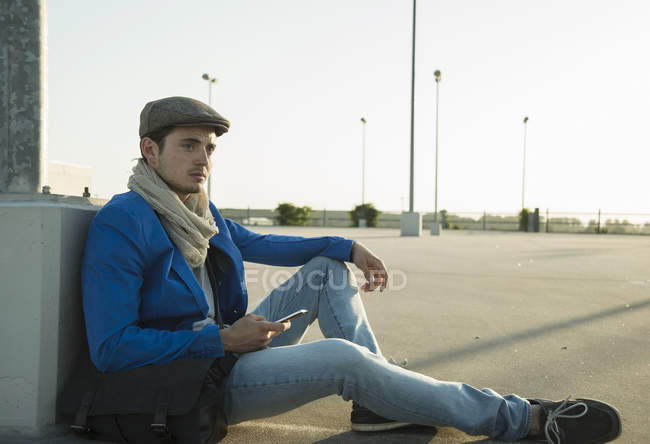 Jovem com smartphone esperando no estacionamento vazio — Fotografia de Stock