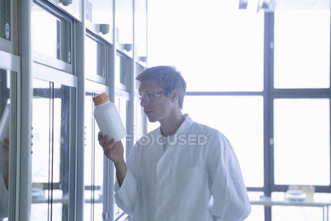 Giovane scienziato maschio guardando bottiglia di plastica in laboratorio — Foto stock