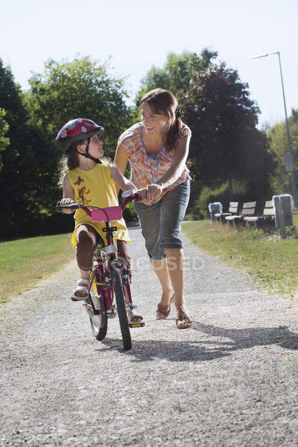 Маленькая девочка учится кататься на велосипеде с мамой — стоковое фото