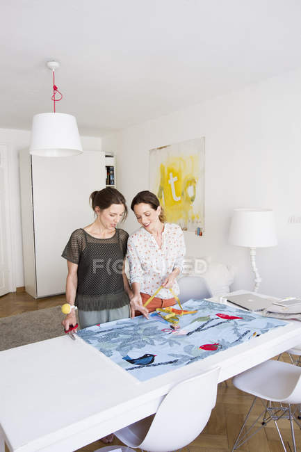 Mulheres maduras em pé na mesa medindo tecido colorido — Fotografia de Stock