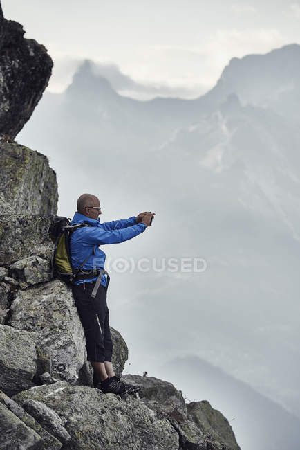 Uomo maturo sulle rocce che scatta foto, Vallese, Svizzera — Foto stock