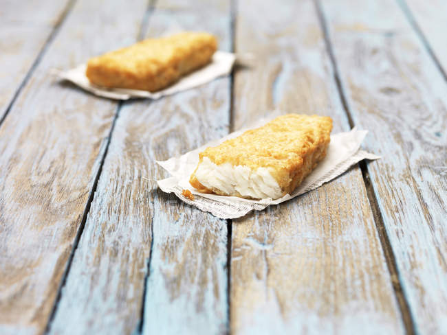 Two fried chunky battered haddock pieces on wooden table — Stock Photo