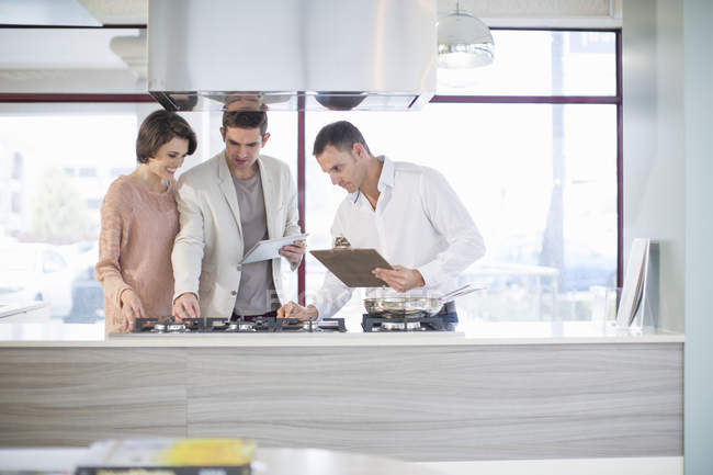 Couple adulte moyen et vendeur regardant plaque de cuisson dans le showroom de la cuisine — Photo de stock