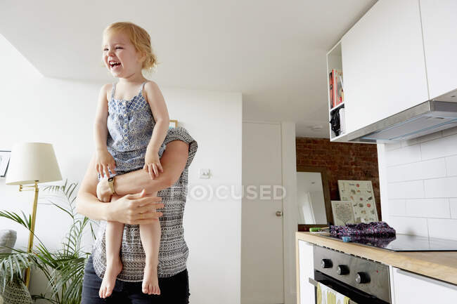 Жінка піднімає дочку малюка на кухні — стокове фото