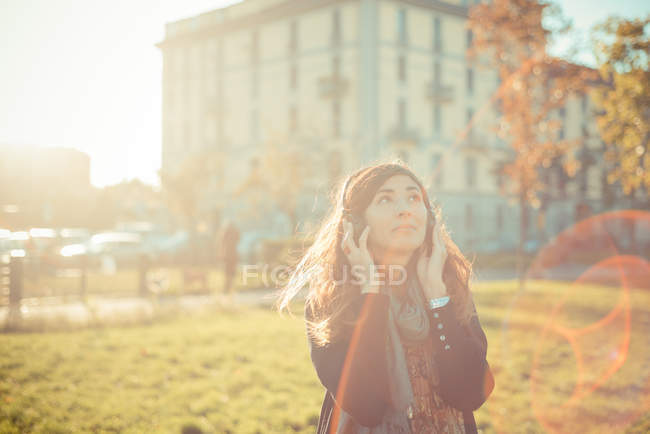 Mid adult woman listening to headphones in sunlit park — Stock Photo