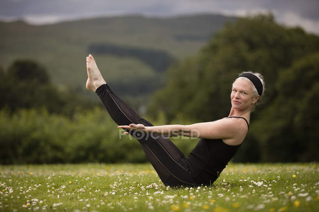 Mature woman practicing yoga boat pose in field — Stock Photo