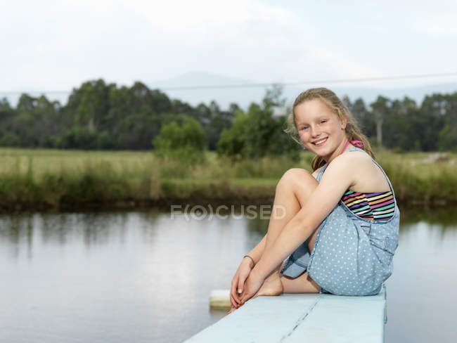 Girl sitting on diving board over lake — Stock Photo