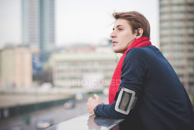 Young male runner looking out over city from rooftop — Stock Photo